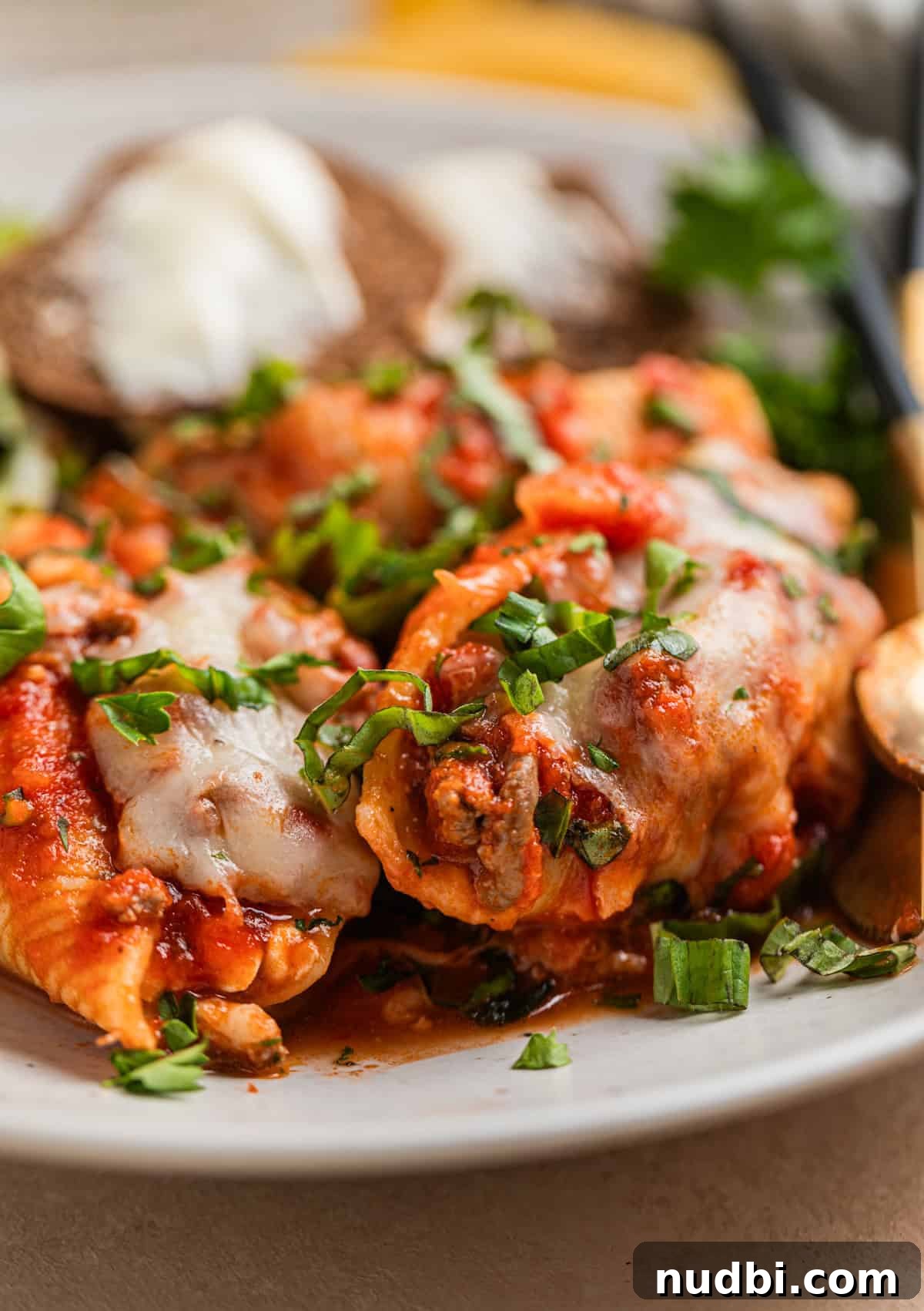 Cheesy Ground Beef Stuffed Shells Recipe for Family Dinners 3 Plate with stuffed shells with ground beef topped with melted mozzarella and chopped parsley and basil.