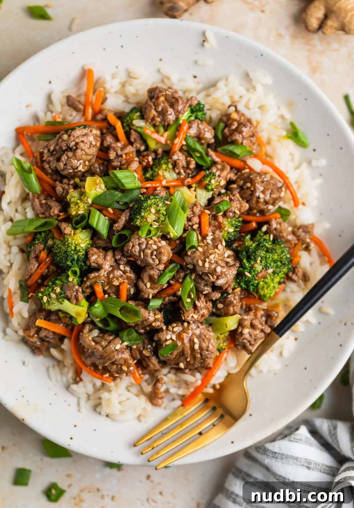 Plate with ground beef teriyaki with broccoli and carrots served over rice and topped with sesame seeds.