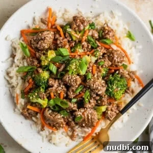 White plate with beef teriyaki served over white rice and topped with chopped green onions and toasted sesame seeds.