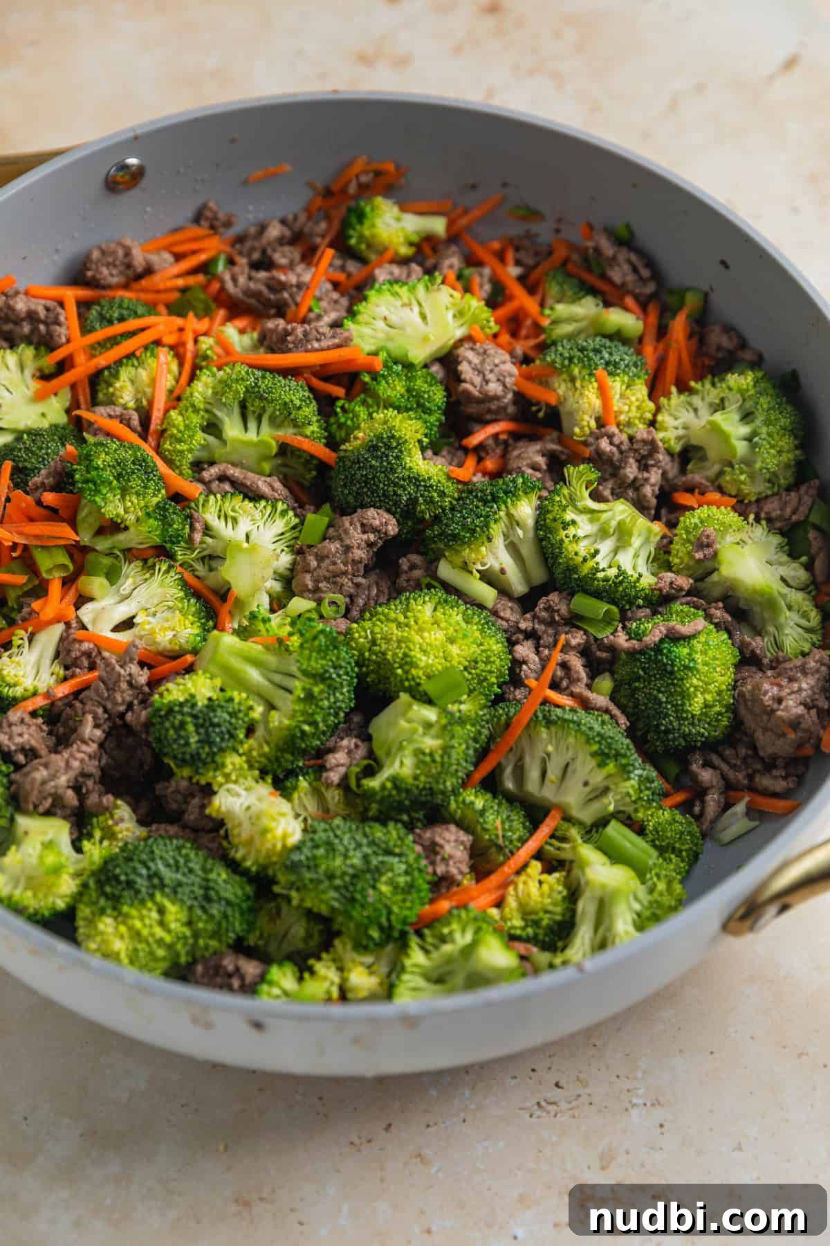 Fresh broccoli florets and shredded carrots added to skillet with browned ground beef.
