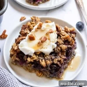Slice of blueberry baked oatmeal on white plate with maple syrup.