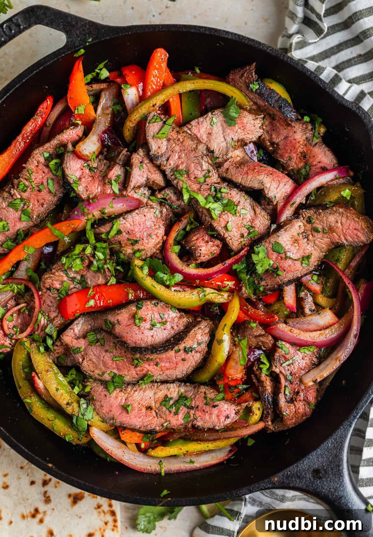 Cilantro-Lime Flat Iron Steak Fajitas Recipe 2 Cast iron skillet with flat iron steak fajitas with onions and peppers topped with chopped cilantro.