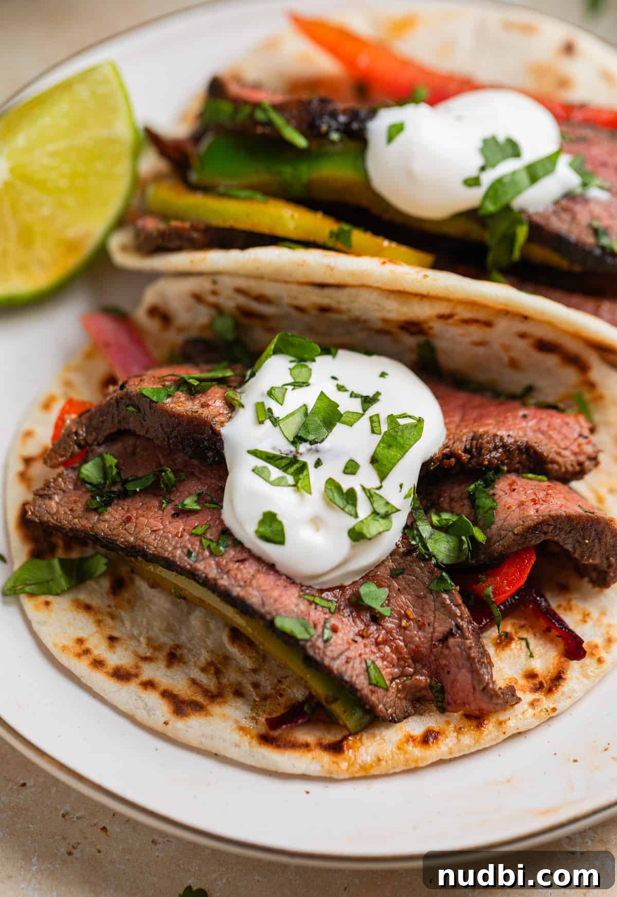 Cilantro-Lime Flat Iron Steak Fajitas Recipe 11 Steak fajitas served on flour tortillas topped with sour cream on plate.