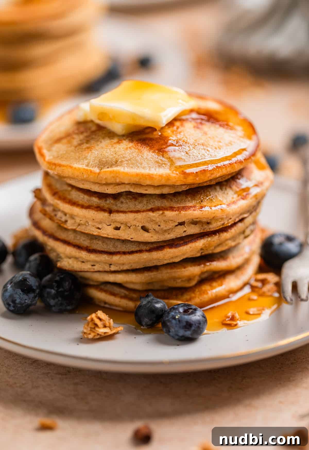 Fluffy Banana Oat Blender Pancakes in Minutes 3 Stack of banana oat pancakes with butter and maple syrup and blueberries and granola on the plate.