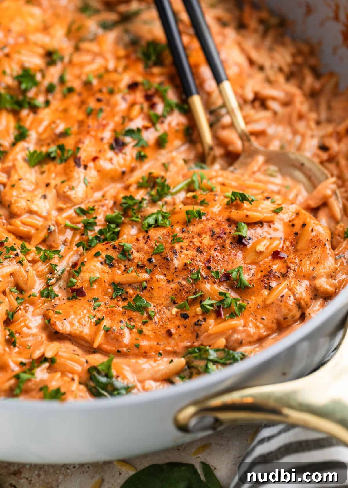 Creamy Chicken Orzo Skillet with Garlic and Parmesan 2 Chicken breast in a creamy tomato orzo in skillet with spoons and topped with chopped parsley.