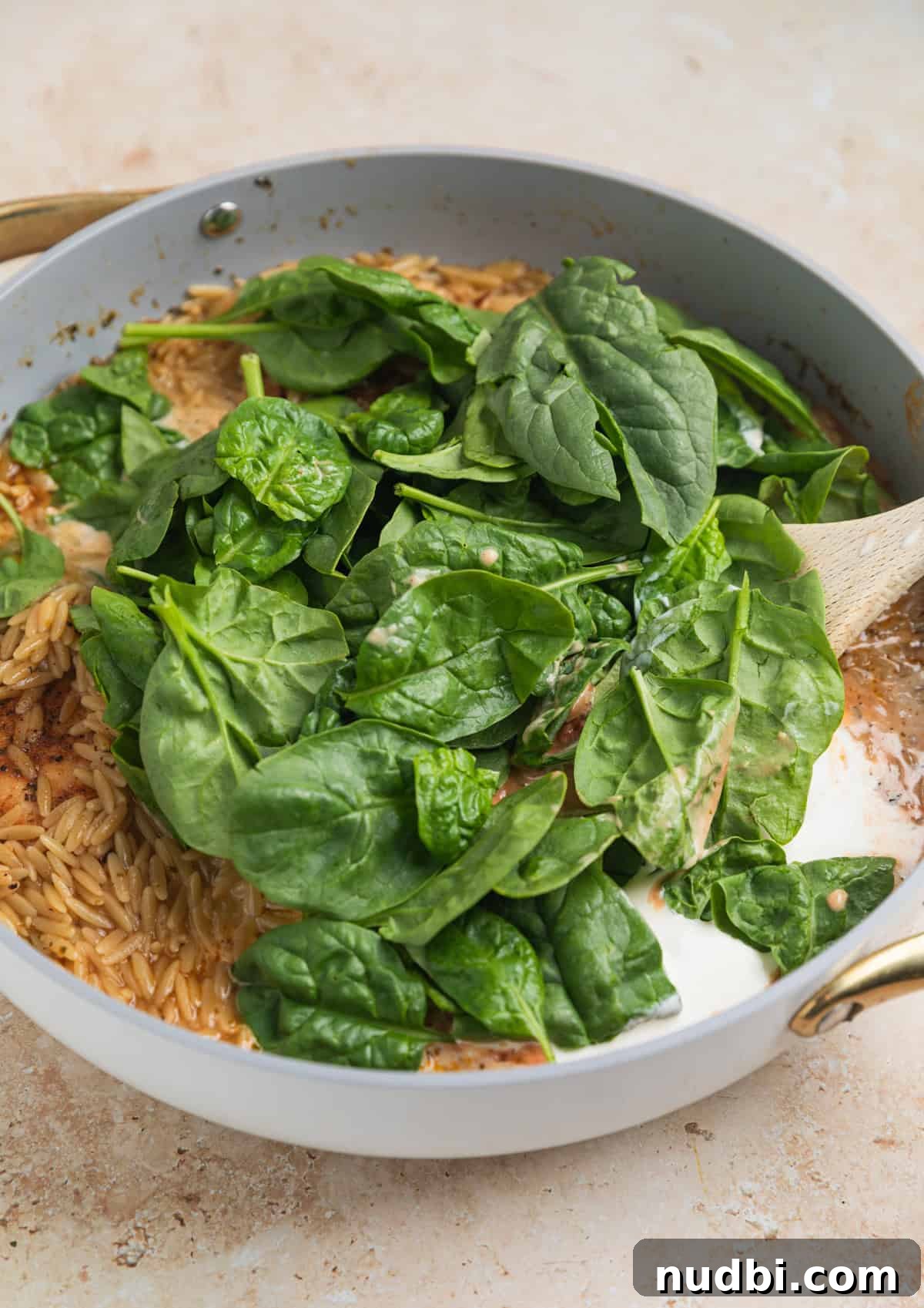 Creamy Chicken Orzo Skillet with Garlic and Parmesan 7 Baby spinach, cream and parmesan added to pot with wooden spoon.