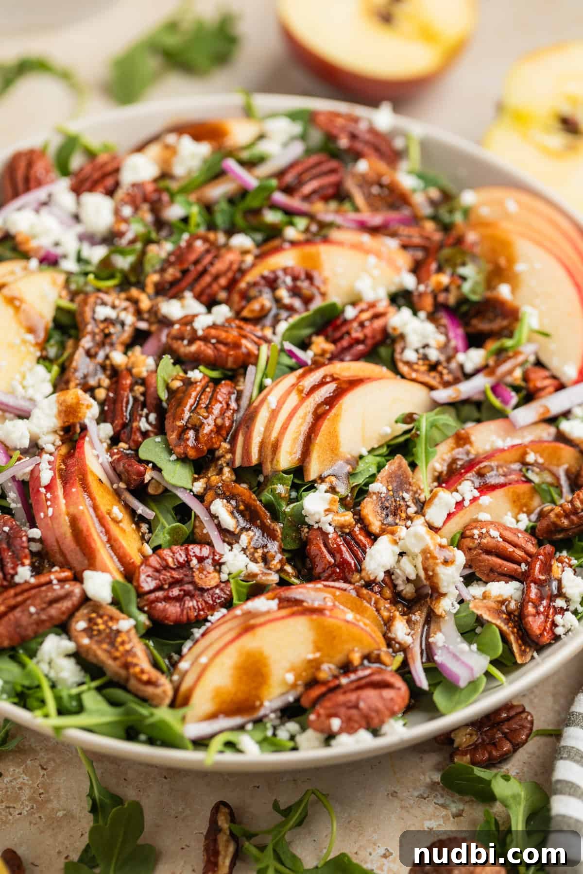 Crisp Apple and Arugula Salad with Honey Dijon Dressing 8 Arugula apple fall salad in bowl with balsamic dressing drizzled over, sliced apple halves and greens arranged around the bowl.