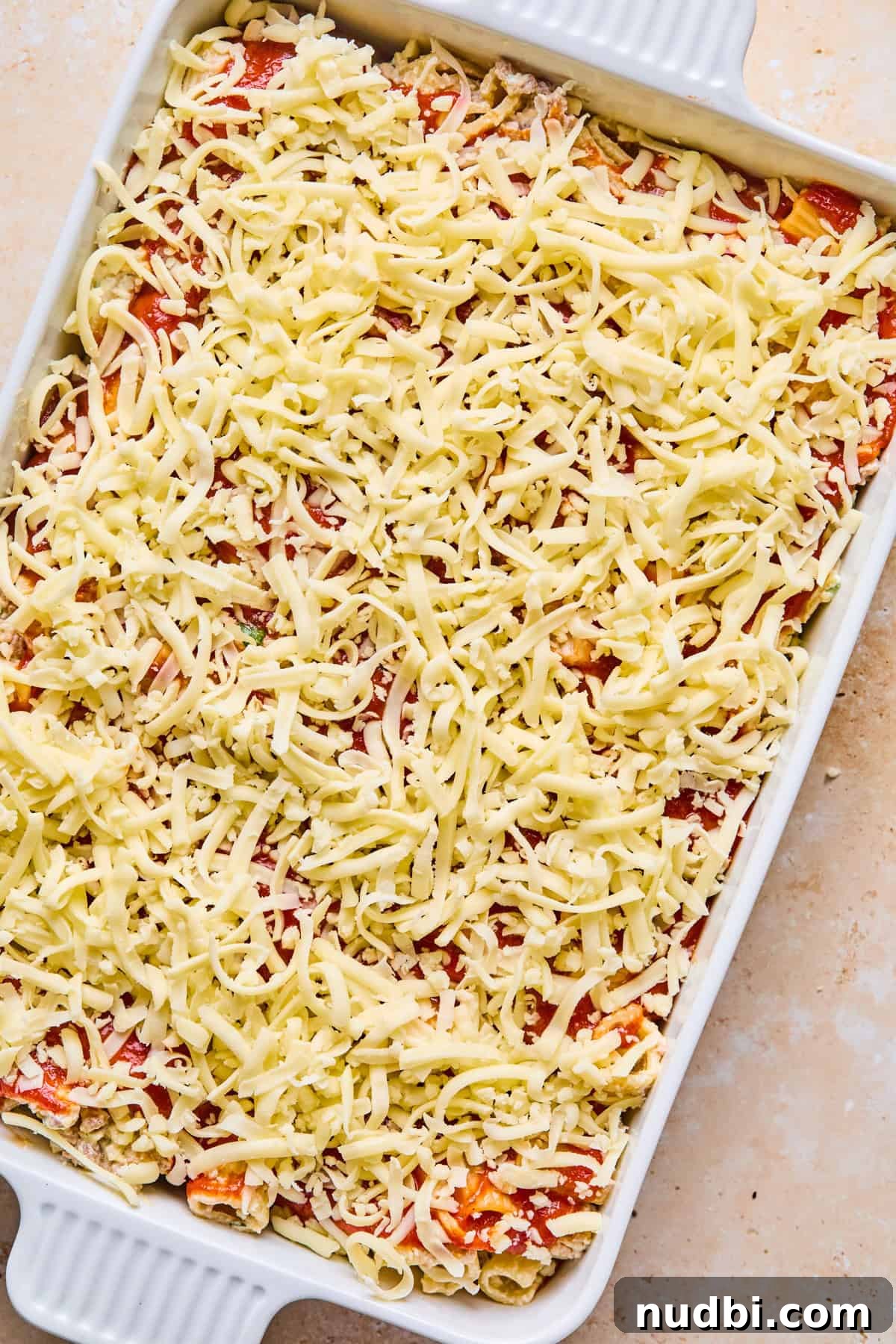 Cheesy Italian Sausage Pasta Bake with Roasted Tomatoes 13 Shredded mozzarella covering top of pasta bake in pan before cooking.