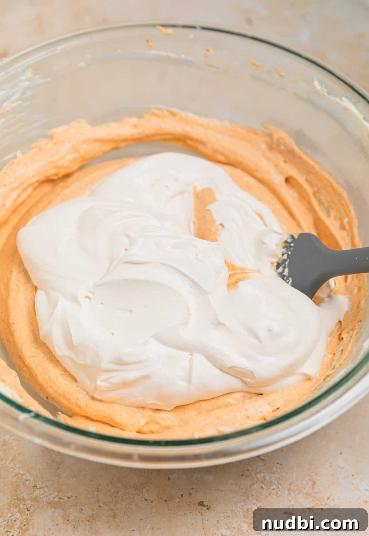 No-Bake Pumpkin Cheesecake Bars Recipe — Creamy Autumn Dessert 7 Whipped cream added to pumpkin cream cheese mixture in bowl with spatula.
