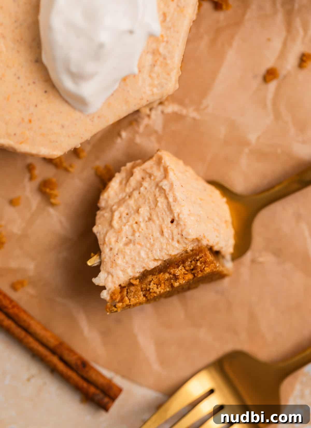No-Bake Pumpkin Cheesecake Bars Recipe — Creamy Autumn Dessert 8 Fork with piece of pumpkin cheesecake resting on it and cinnamon stick and fork surrounding.