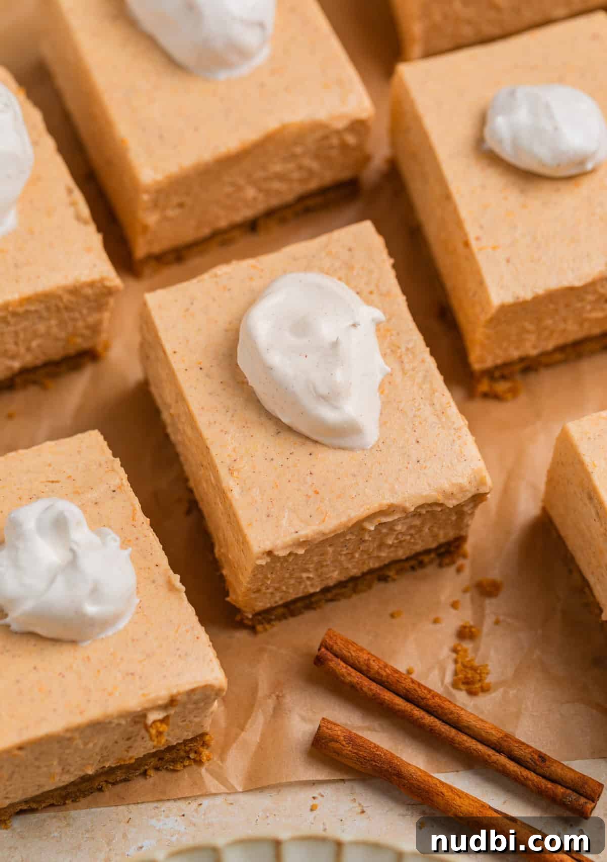 No-Bake Pumpkin Cheesecake Bars Recipe — Creamy Autumn Dessert 9 Slices of no bake pumpkin cheesecake on parchment with dollop of whipped cream on top.