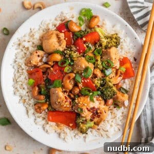Baked cashew chicken over rice on plate with chopsticks.
