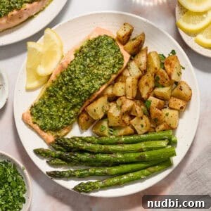 Pesto salmon dinner on white plate with potatoes, asparagus and two lemon slices.