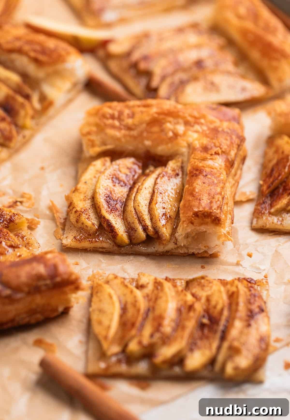 Crisp Puff Pastry Apple Tart Recipe for Homemade Dessert 2 Puff pastry and apple tarts sliced and arranged on parchment with cinnamon sticks surrounding.