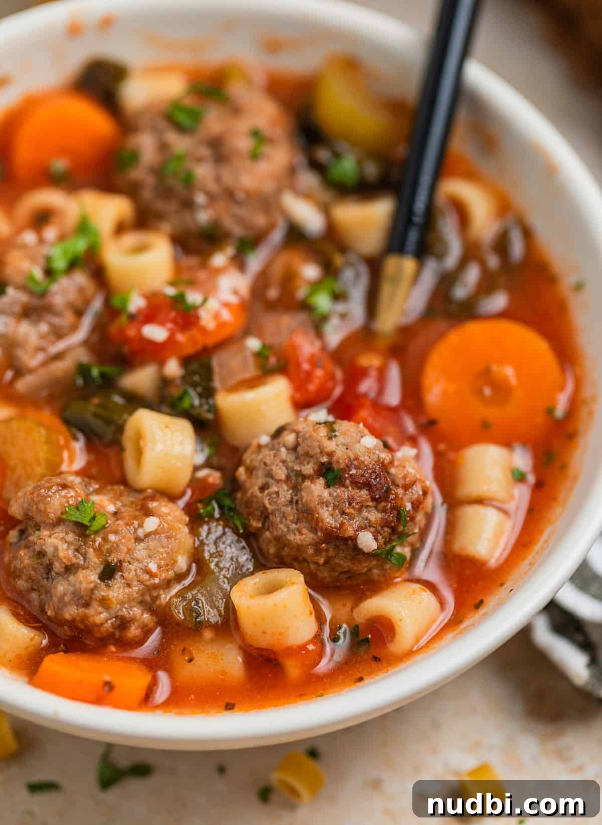 Hearty Vegetable and Meatball Soup Recipe for Cozy Meals 7 Spoon scooping into bowl with meatball soup topped with grated parmesan and parsley.
