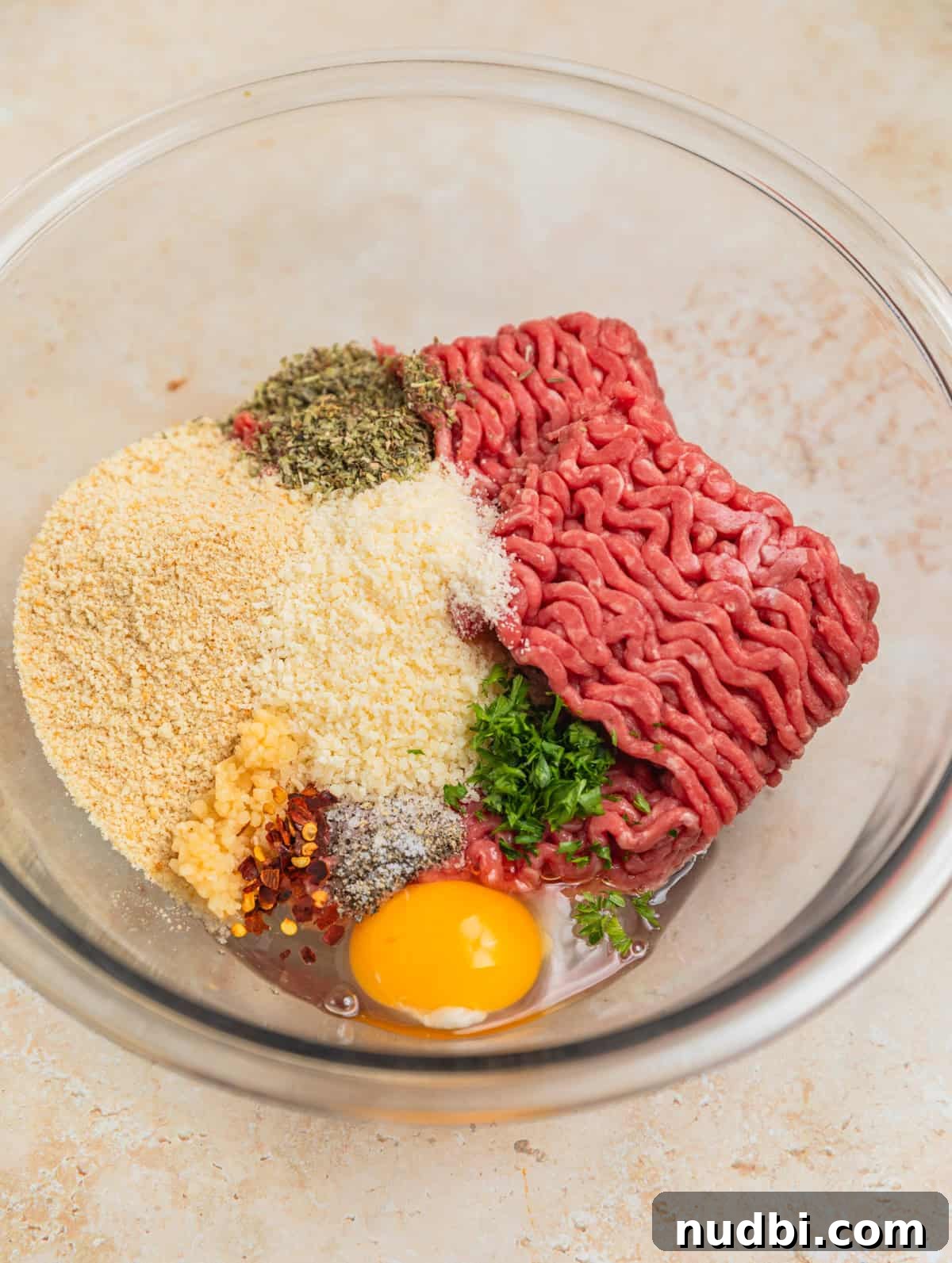 Hearty Vegetable and Meatball Soup Recipe for Cozy Meals 3 Ground sirloin, breadcrumbs, egg, parsley and other meatball ingredients in glass mixing bowl.