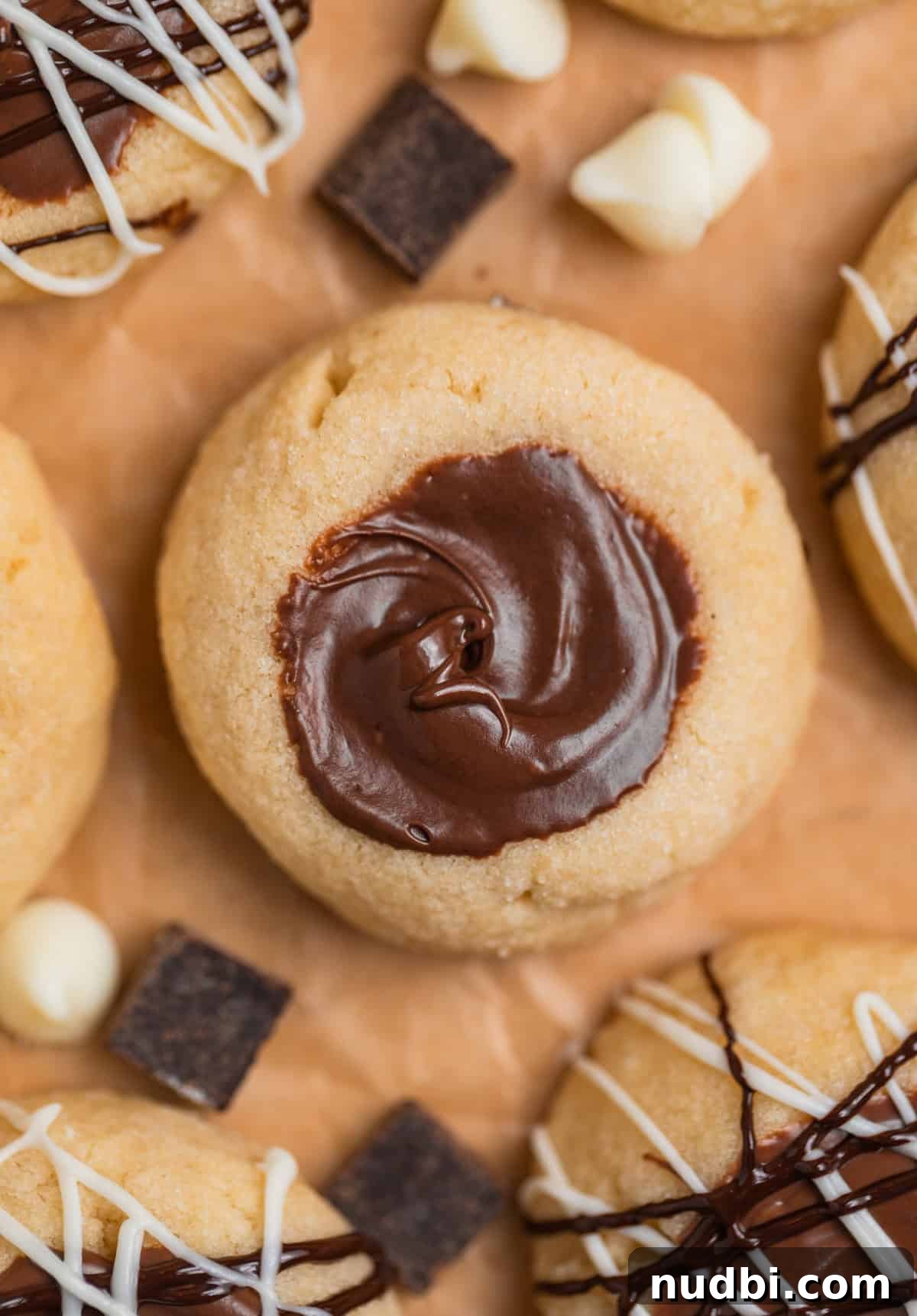Nutella Thumbprint Cookies Recipe — Gooey Chocolate Hazelnut Treats 2 Nutella thumbprint cookies arranged on parchment with dark and white chocolate chips sprinkled around.