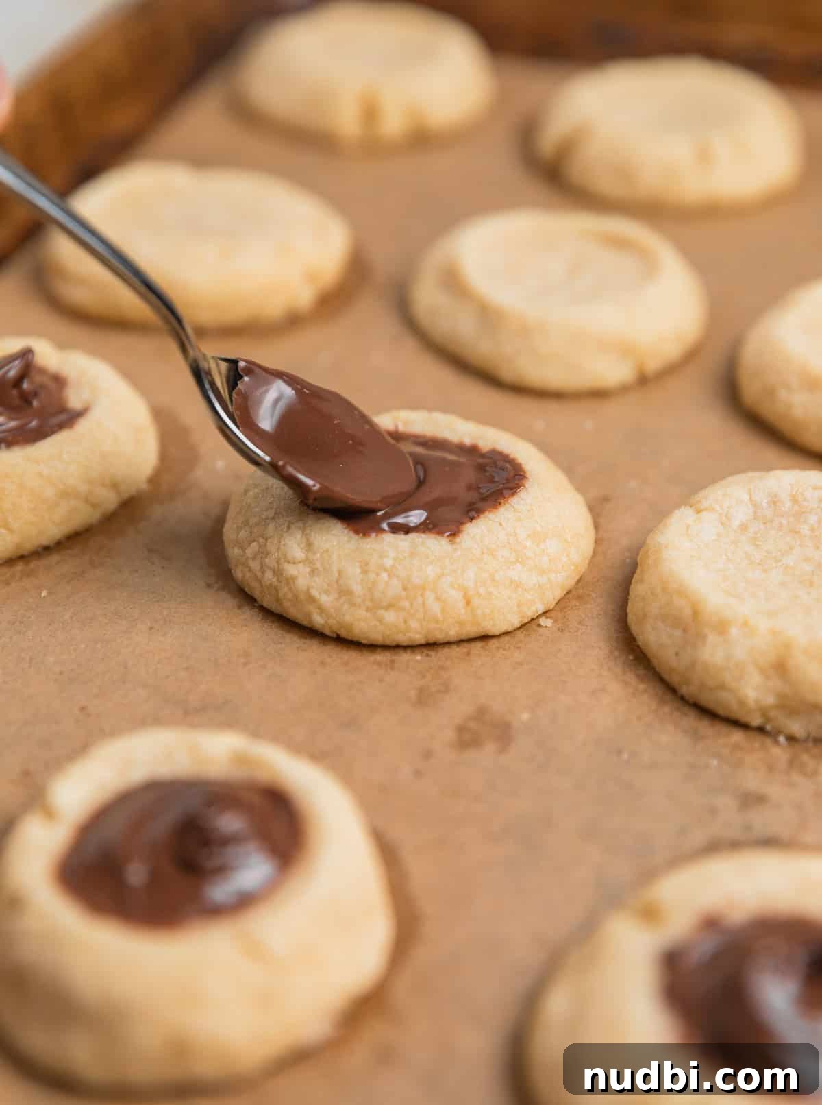 Nutella Thumbprint Cookies Recipe — Gooey Chocolate Hazelnut Treats 12 Nutella spooned into thumbprint impressions of cookies on sheet pan.