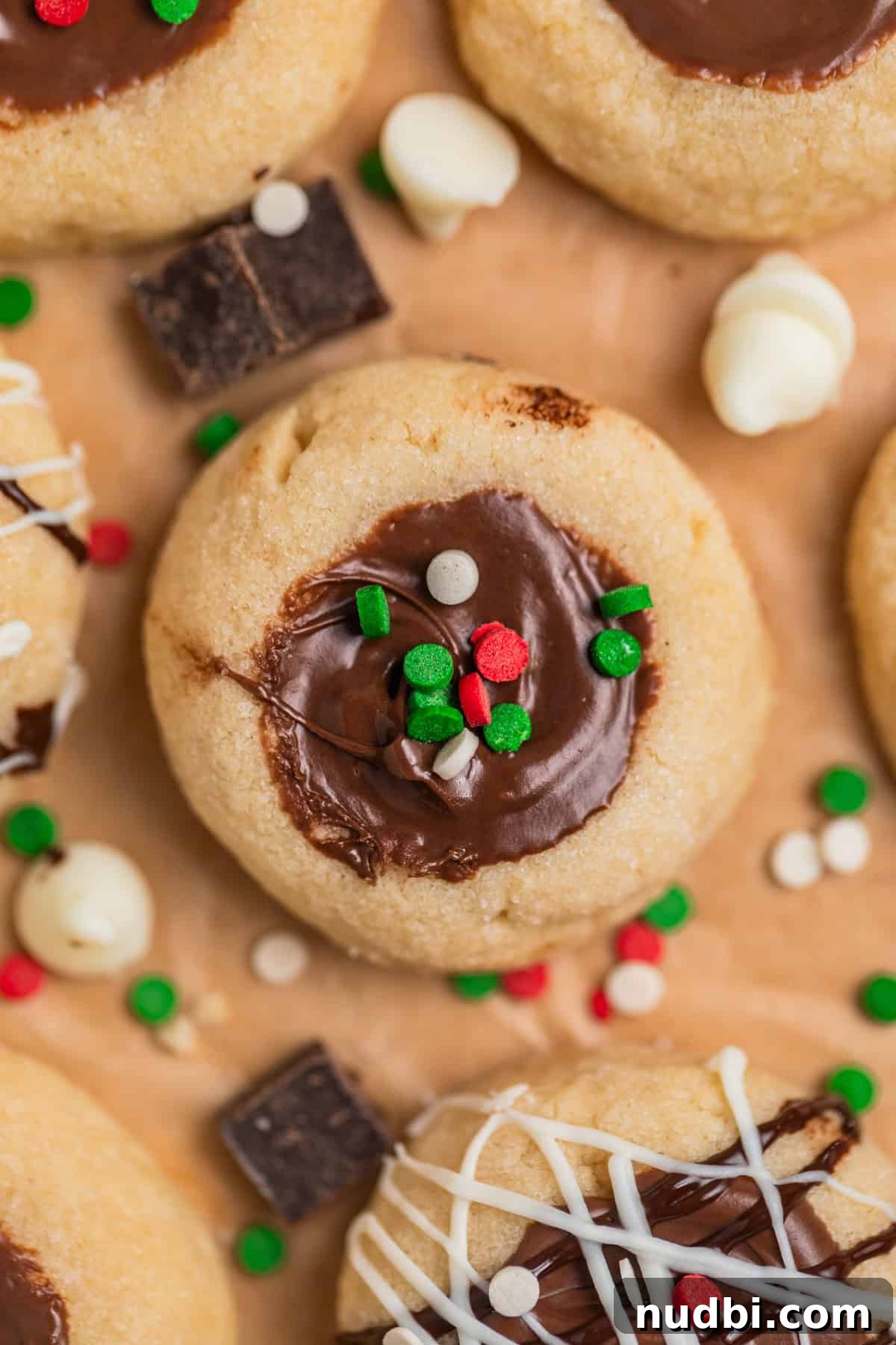 Nutella Thumbprint Cookies Recipe — Gooey Chocolate Hazelnut Treats 13 Nutella thumbprint cookies arranged on parchment with red, white and green holiday sprinkles on top.