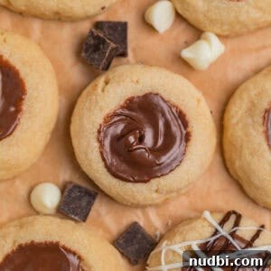 Nutella Thumbprint Cookies Recipe — Gooey Chocolate Hazelnut Treats 18 Nutella cookies arranged on parchment with white and dark chocolate chips arranged around the cookies.