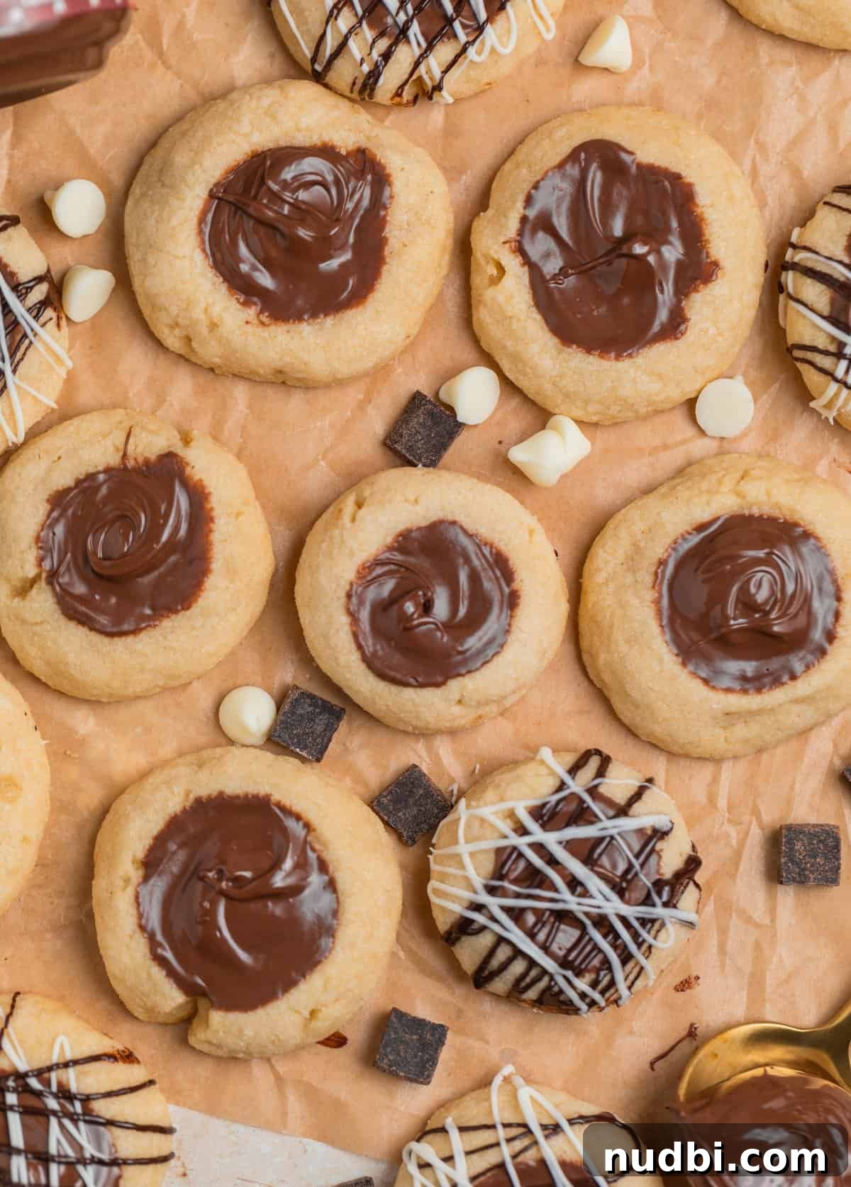 Nutella Thumbprint Cookies Recipe — Gooey Chocolate Hazelnut Treats 3 Nutella thumbprint cookies on brown parchment with white and dark chocolate drizzle on some of the cookies.