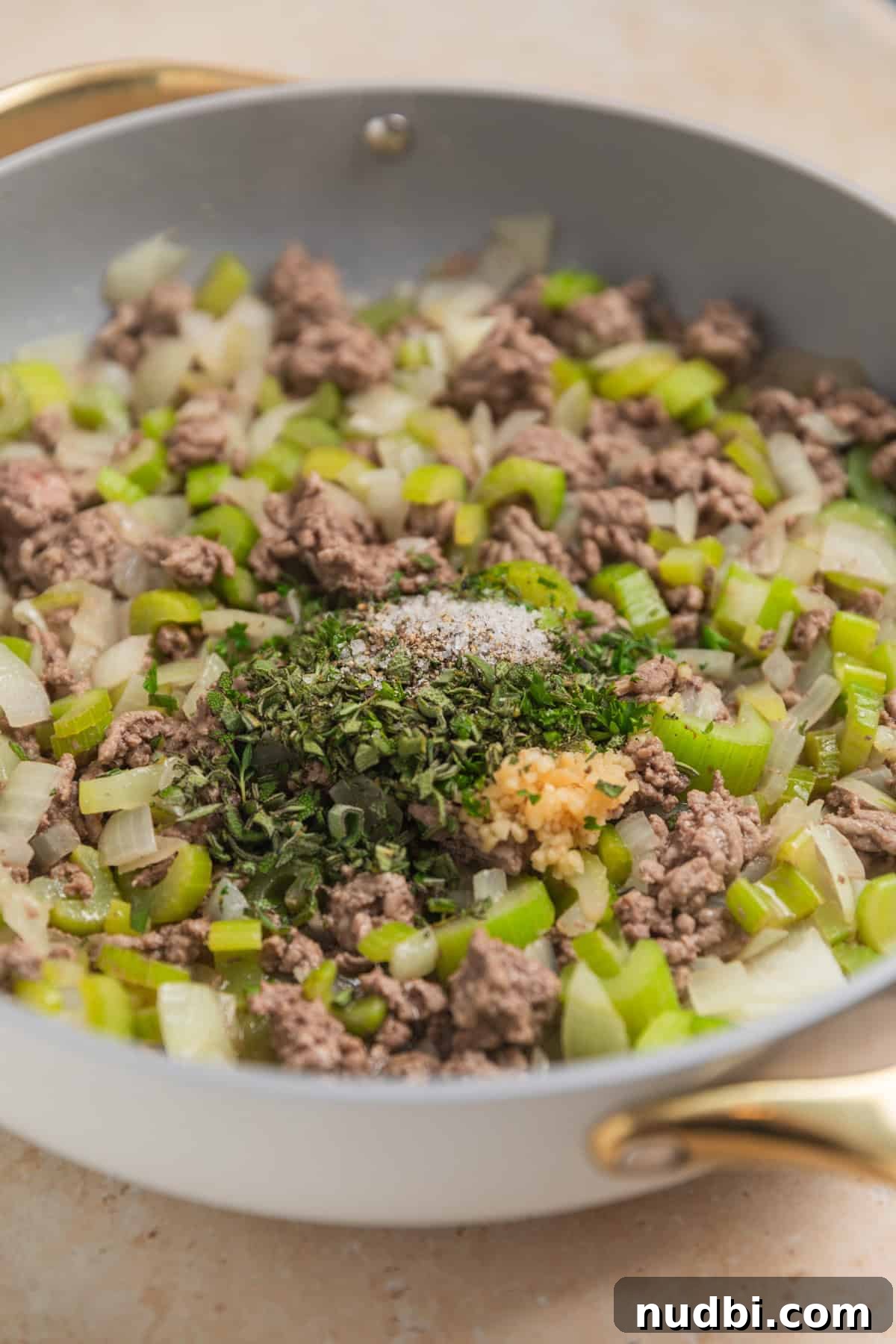 Savory Beef and Cornbread Stuffing Recipe for Holiday Dinners 6 Ground beef browned in skillet with onion and celery and herbs on top.