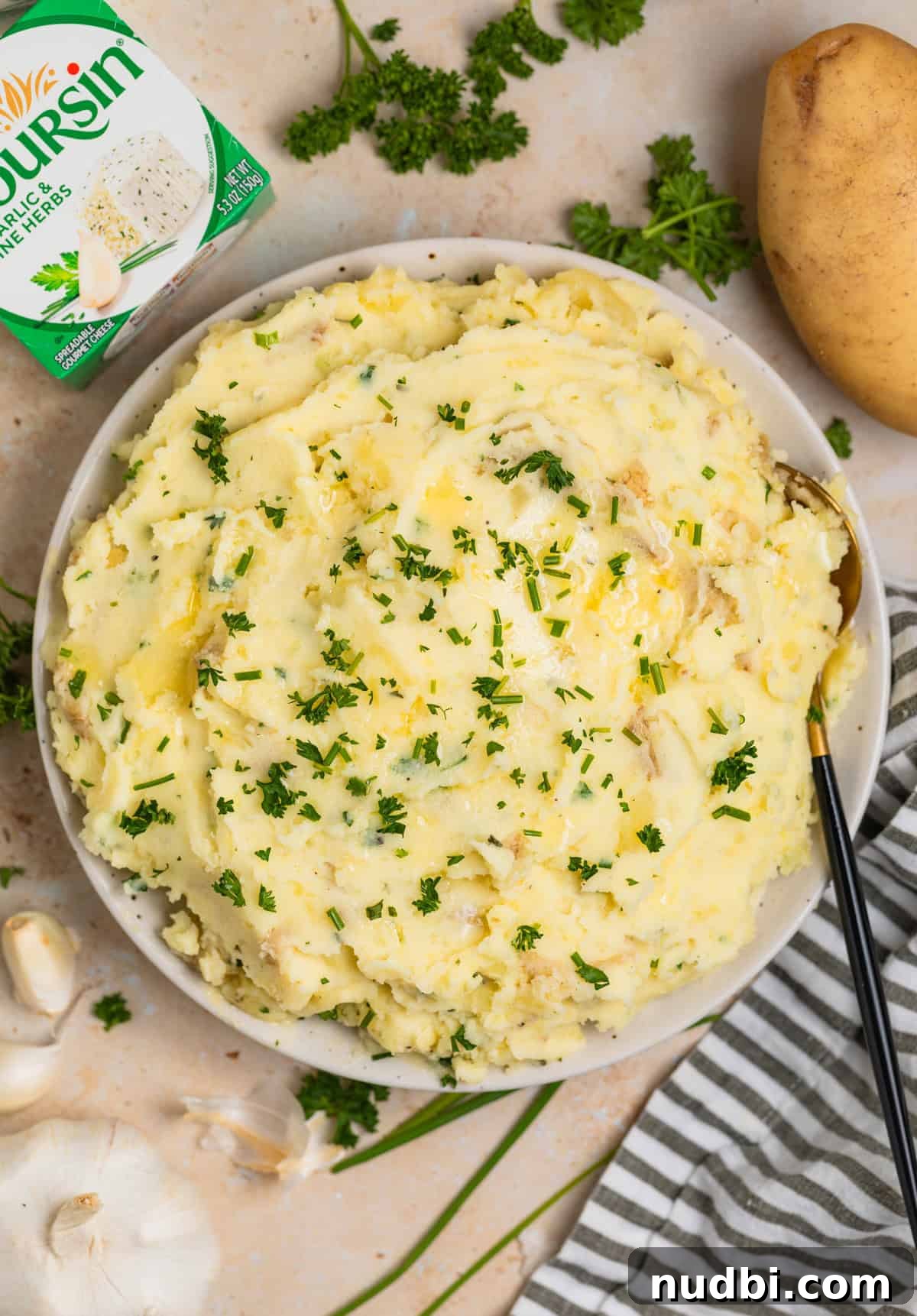 Creamy Boursin Mashed Potatoes Recipe for Garlic-Herb Flavor 2 Boursin mashed potatoes in bowl with serving spoon topped with chives and fresh parsley.
