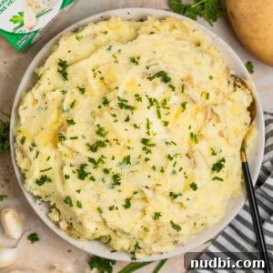 Creamy Boursin Mashed Potatoes Recipe for Garlic-Herb Flavor 8 Serving bowl with Boursin mashed potatoes topped with butter, chives and parsley.