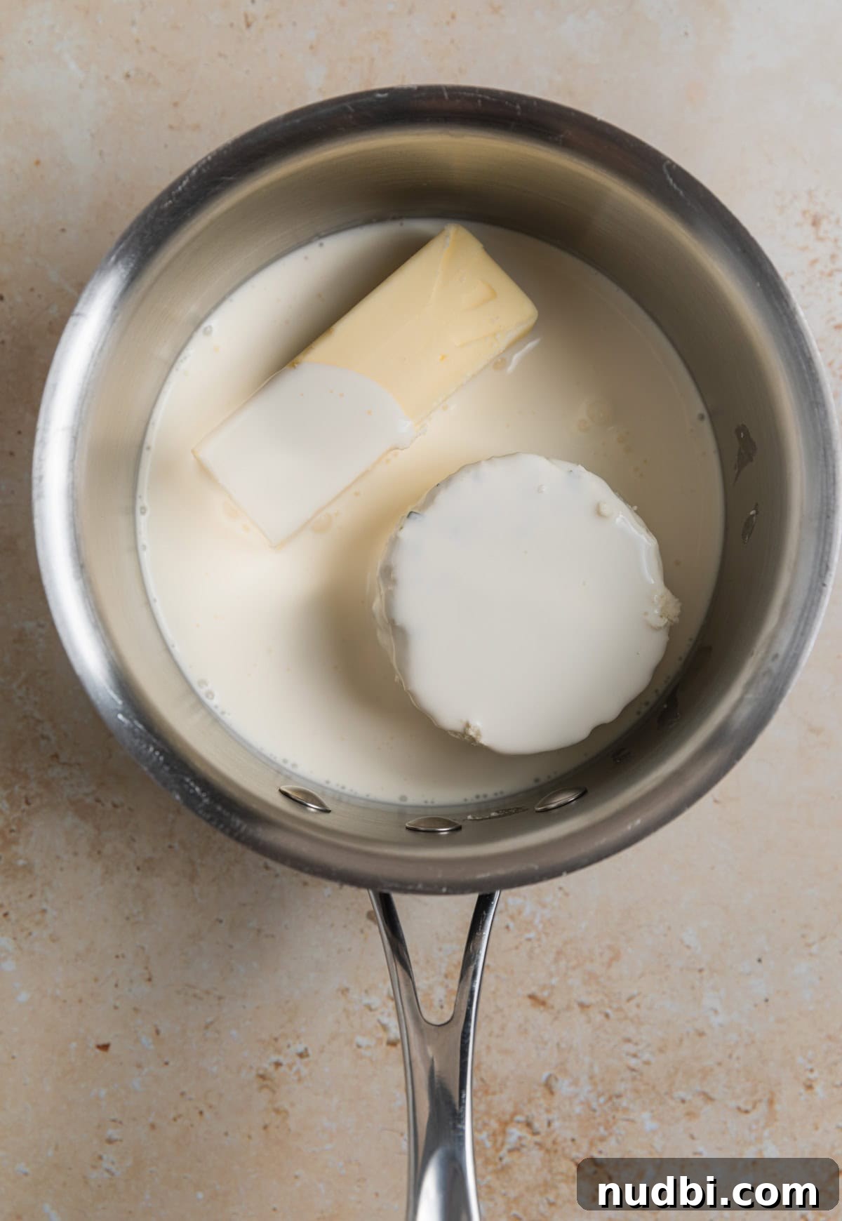 Creamy Boursin Mashed Potatoes Recipe for Garlic-Herb Flavor 5 Pot with cream, butter and Boursin cheese round before being melted.