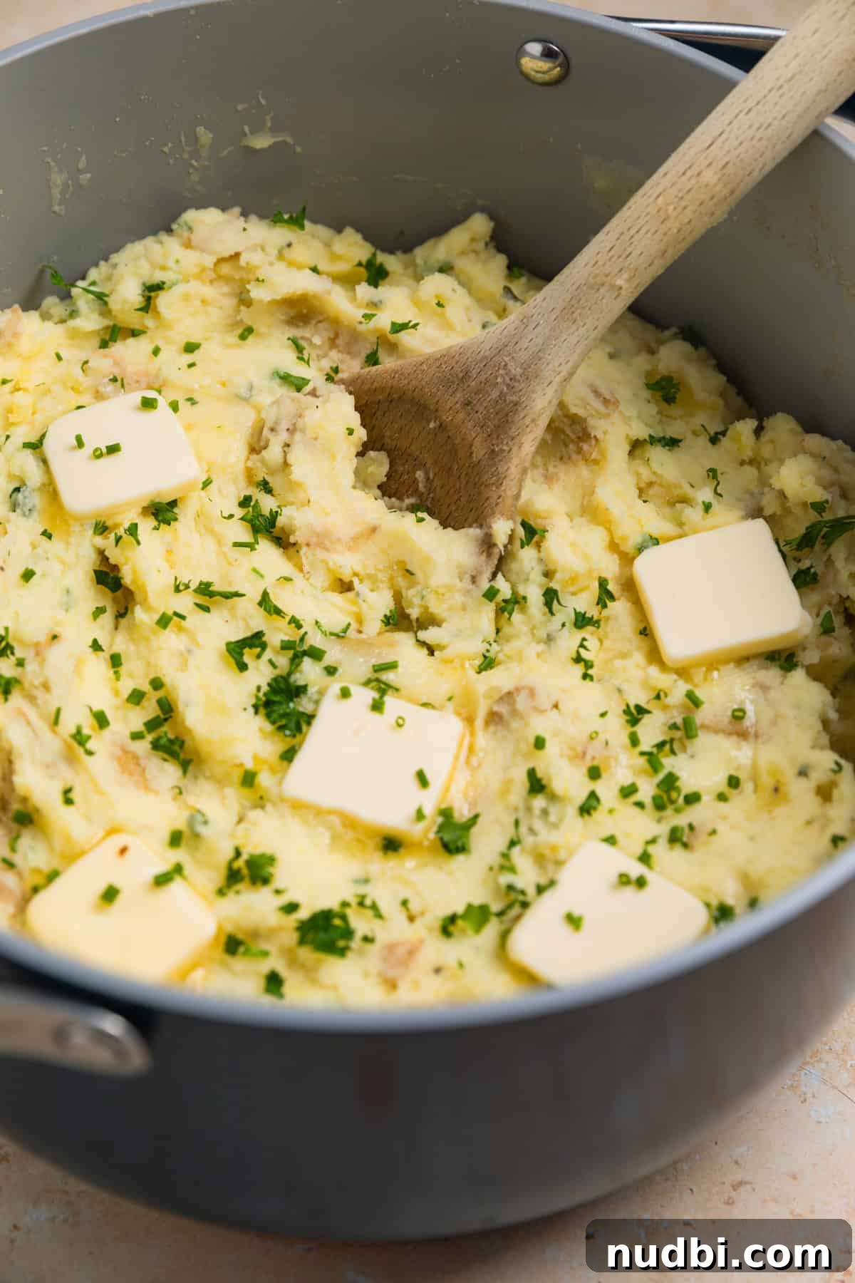 Creamy Boursin Mashed Potatoes Recipe for Garlic-Herb Flavor 7 Pot with prepared mashed potatoes topped with fresh chives, parsley and pats of butter.