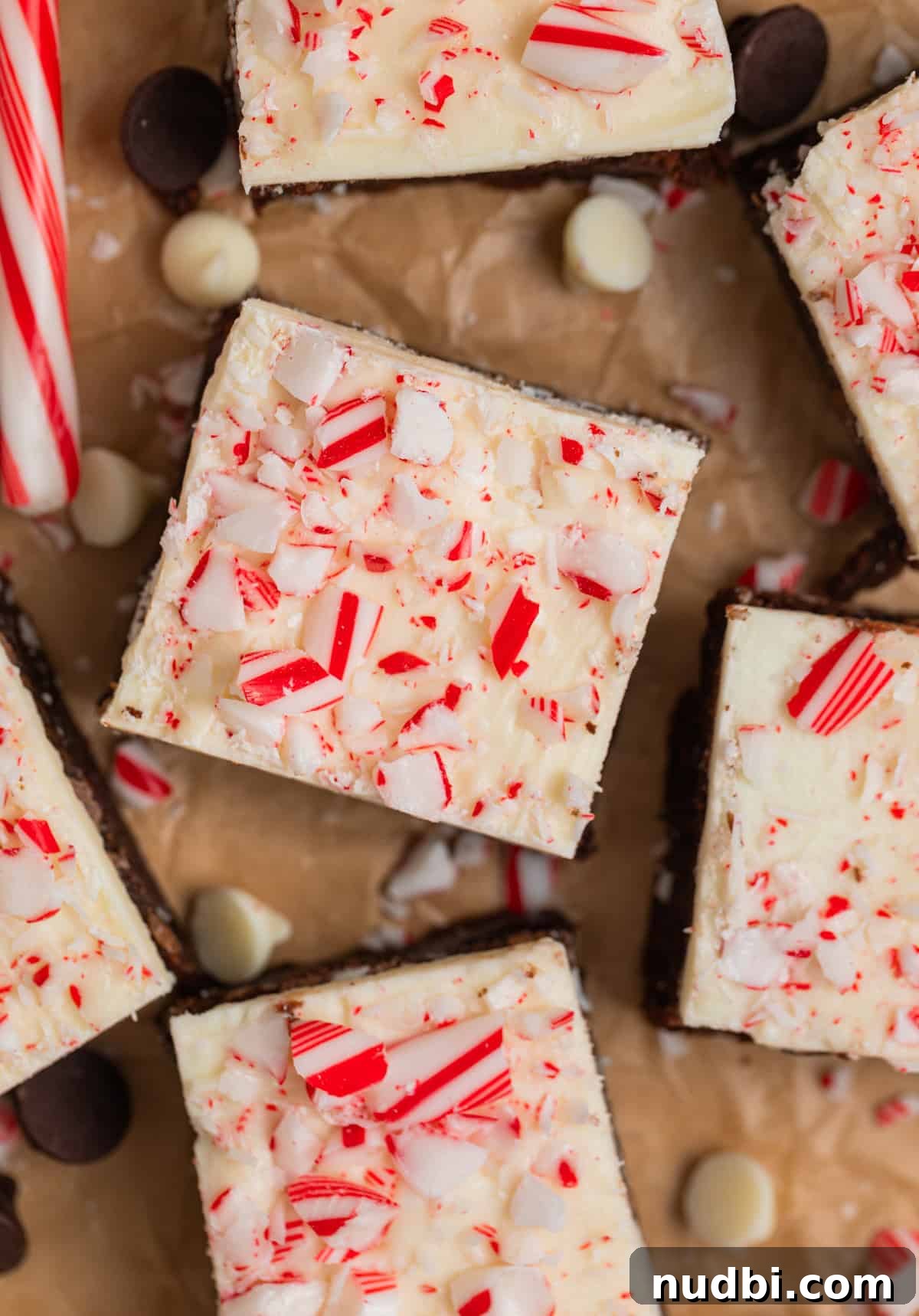Peppermint Bark Brownies Recipe: Fudgy Chocolate Mint Bars 2 Peppermint bark topped brownies with crushed candy canes on top arranged on parchment.