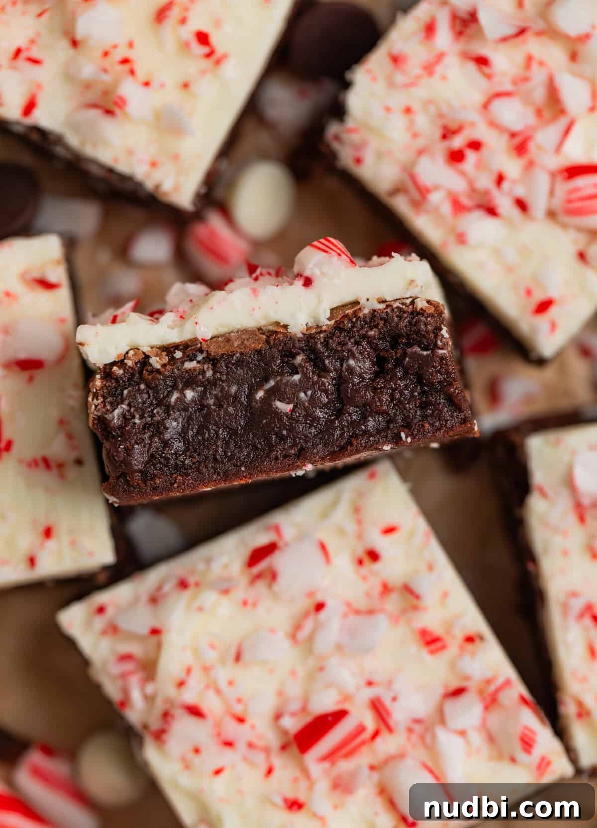 Peppermint Bark Brownies Recipe: Fudgy Chocolate Mint Bars 13 Peppermint bark topped brownies arranged on parchment with one propped on its side to show layers.