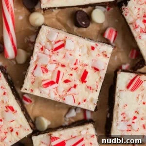 Peppermint Bark Brownies Recipe: Fudgy Chocolate Mint Bars 14 Brownies topped with white chocolate peppermint bark with candy canes and white and dark chocolate chips around them.