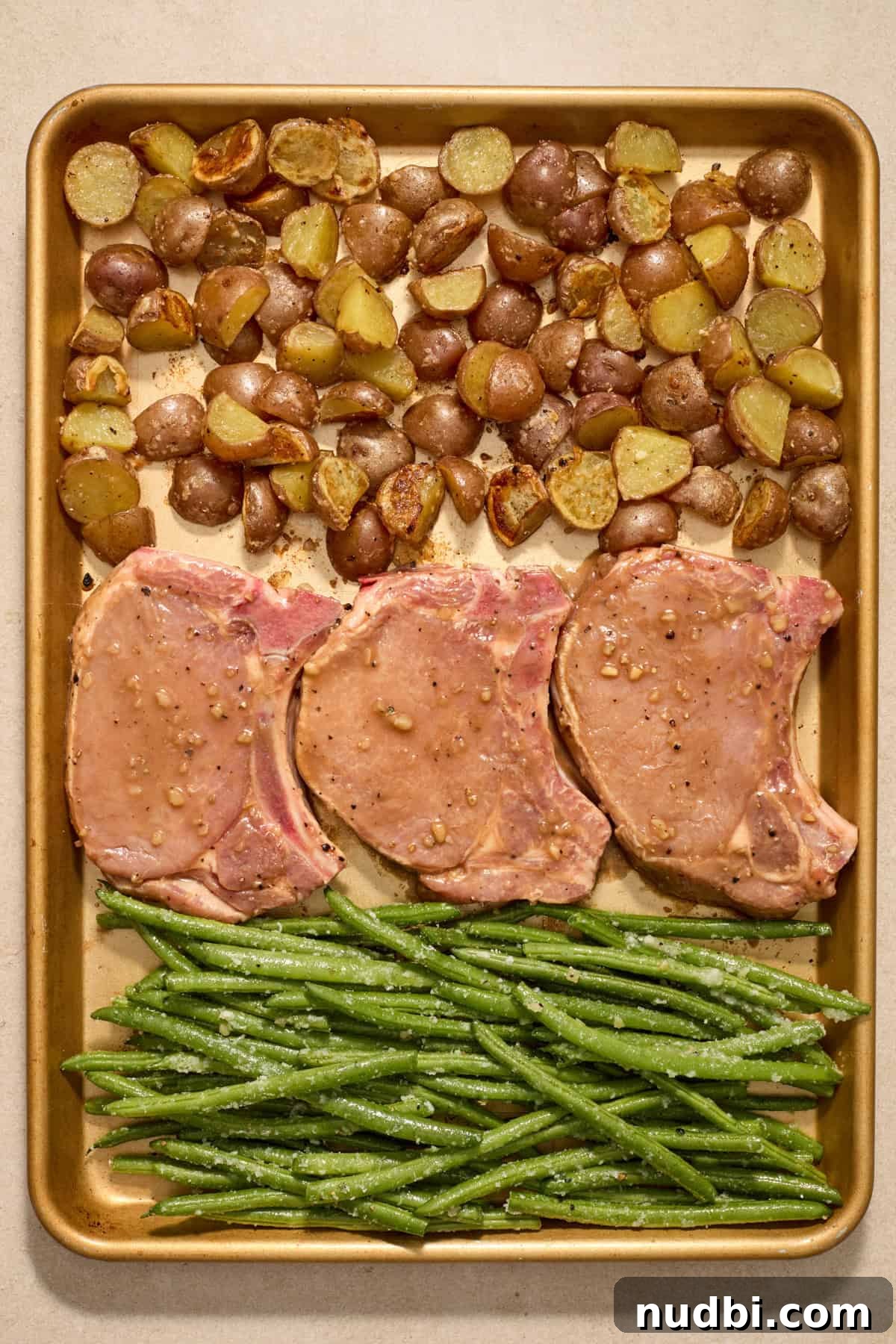 Crispy Sheet Pan Pork Chops with Roasted Vegetables 9 Baking sheet with potatoes, pork chops and green beans before being placed in oven.