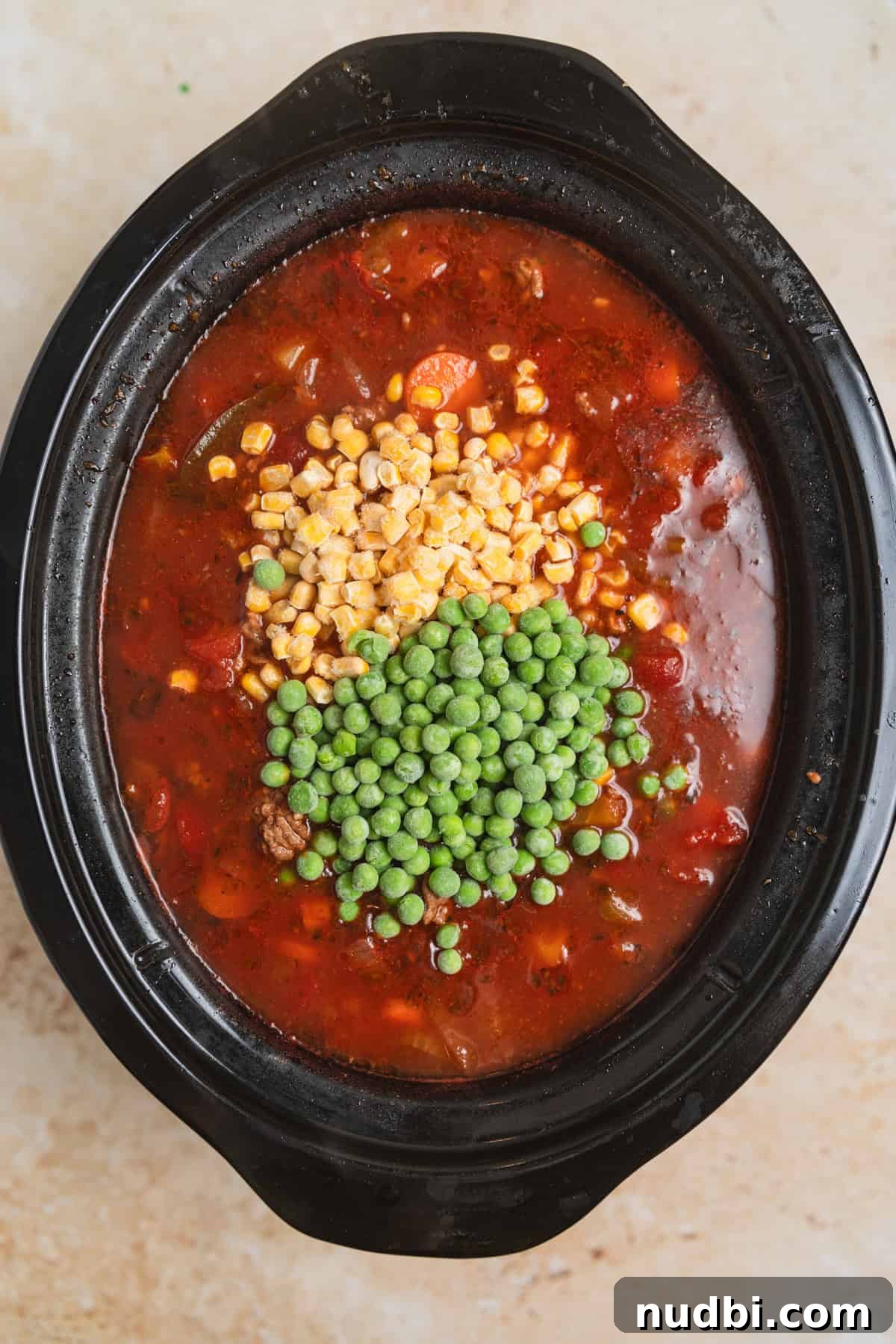 Slow Cooker Hamburger Soup Recipe for Hearty Weeknight Meals 7 Frozen peas and corn added into slow cooker with hamburger soup.