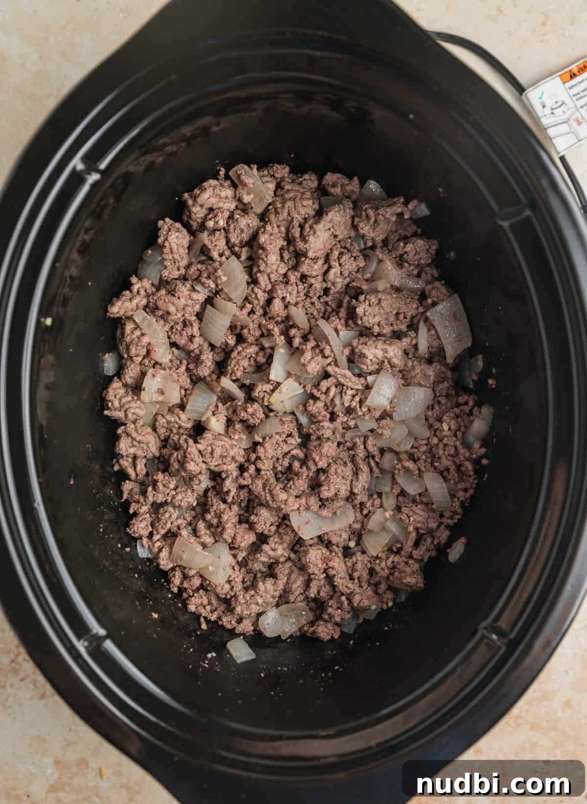Hearty No-Bean Slow Cooker Chili Recipe 4 Crock pot with browned beef and sautéed onions at the bottom.