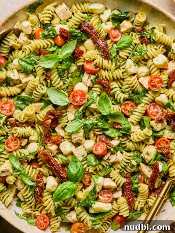 Hearty No-Bean Slow Cooker Chili Recipe 10 Pesto chicken pasta salad in serving bowl topped with fresh basil with serving spoon.