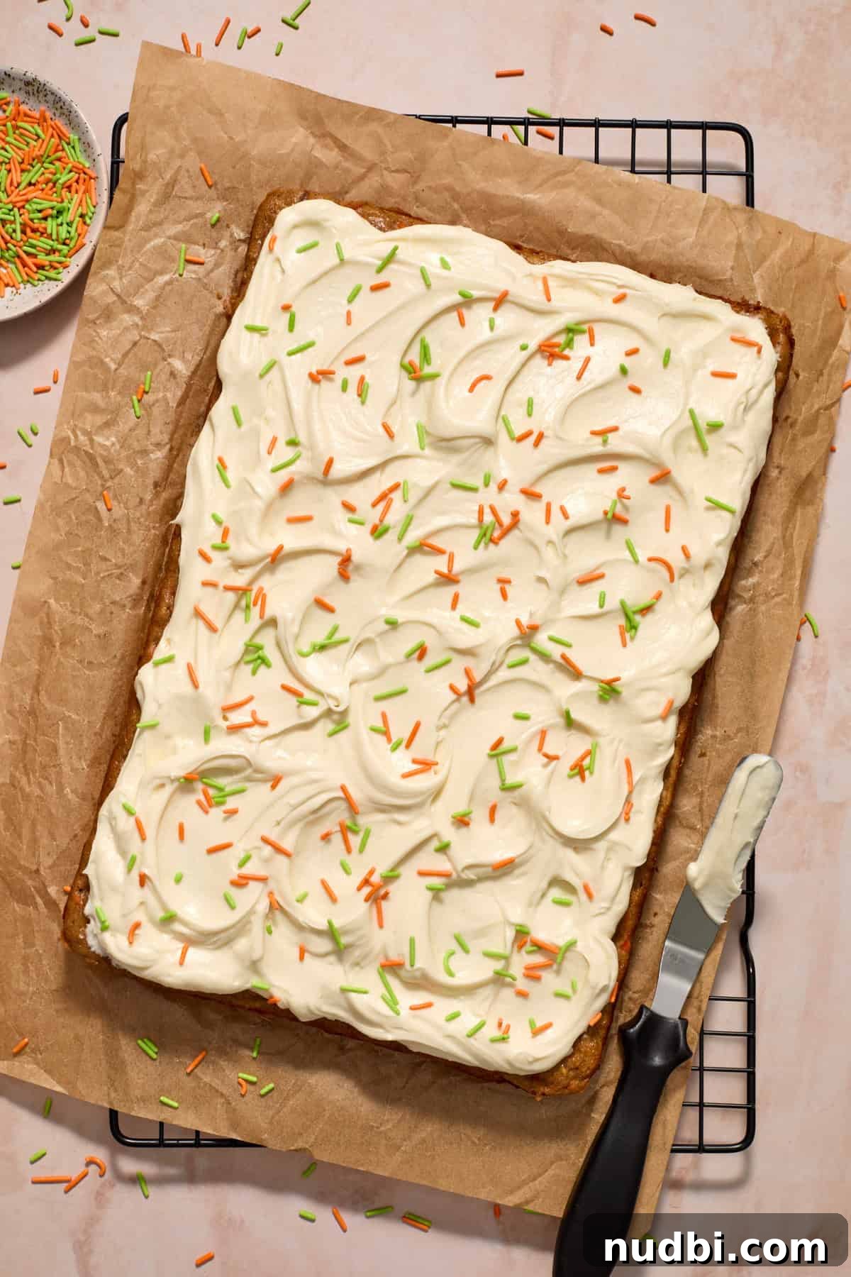 Moist Carrot Cake Recipe Using Cake Mix 11 Cream cheese frosted carrot cake on parchment paper with orange and green sprinkles on top.