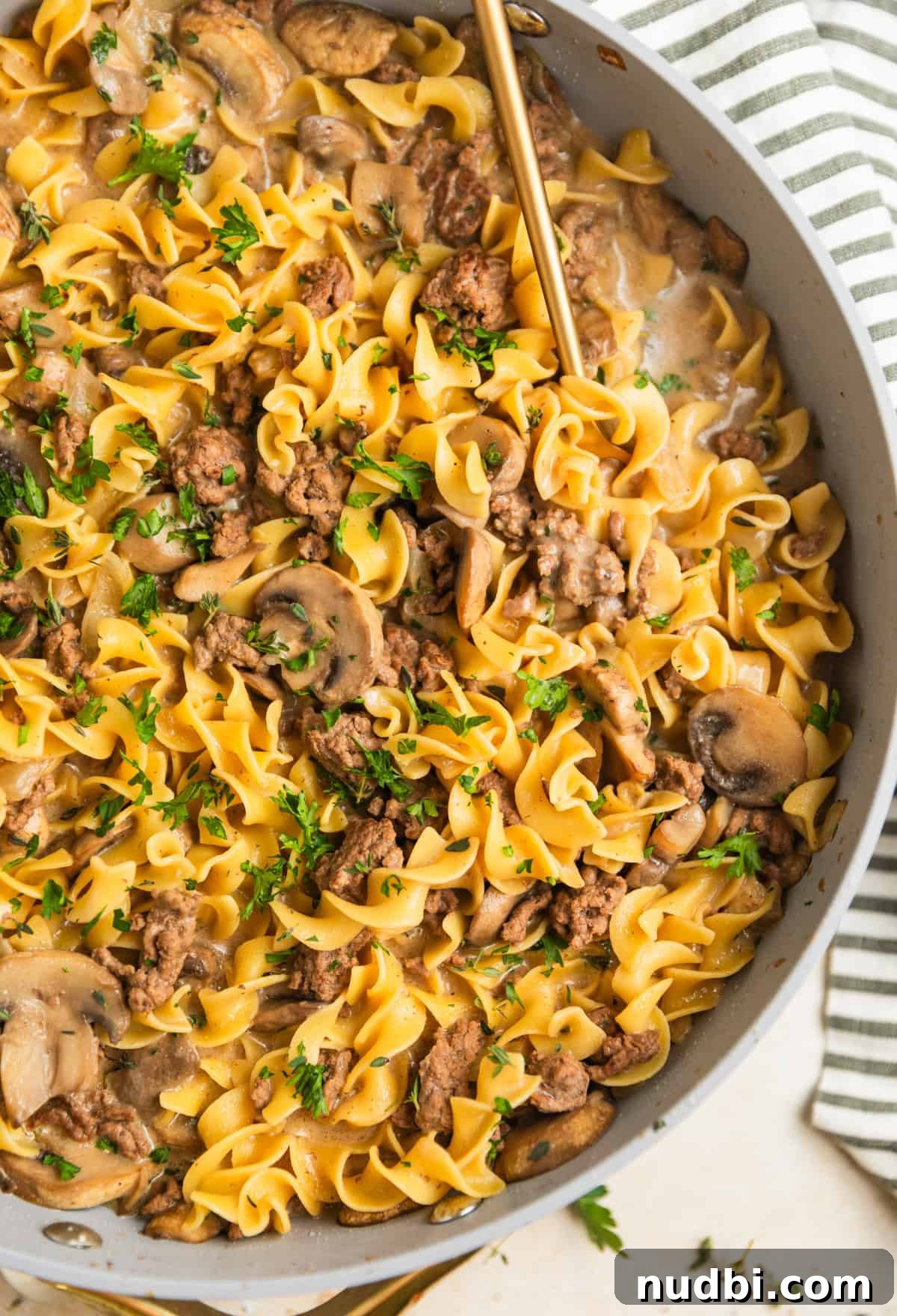 Creamy One-Pot Ground Beef Stroganoff Recipe 2 Skillet with one pot ground beef stroganoff topped with chopped parsley and serving spoon scooping in to the skillet.