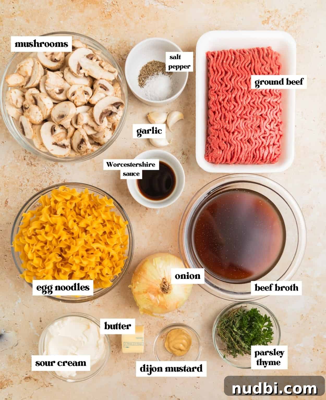 Creamy One-Pot Ground Beef Stroganoff Recipe 3 Mushrooms, beef broth, ground beef, fresh herbs and other ingredients needed to make recipe arranged on surface.