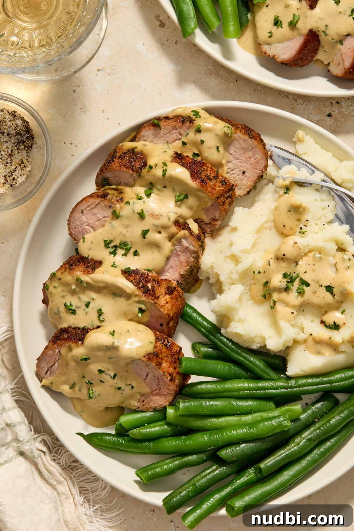 Juicy Pork Tenderloin with Creamy Mustard Sauce receta 10 Plate with sliced pork tenderloin topped with creamy mustard sauce served with mashed potatoes and green beans.