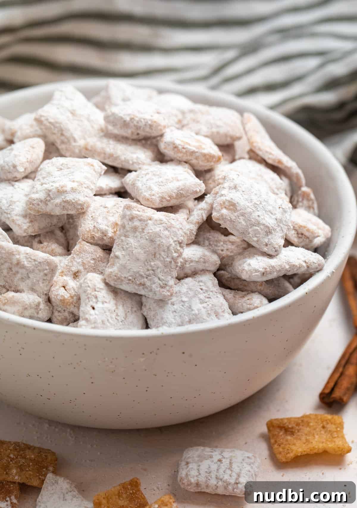 Snickerdoodle Puppy Chow Recipe — Cinnamon Sugar Snack Mix 6 Snickerdoodle puppy chow in bowl with cinnamon stick and cereal beside it.