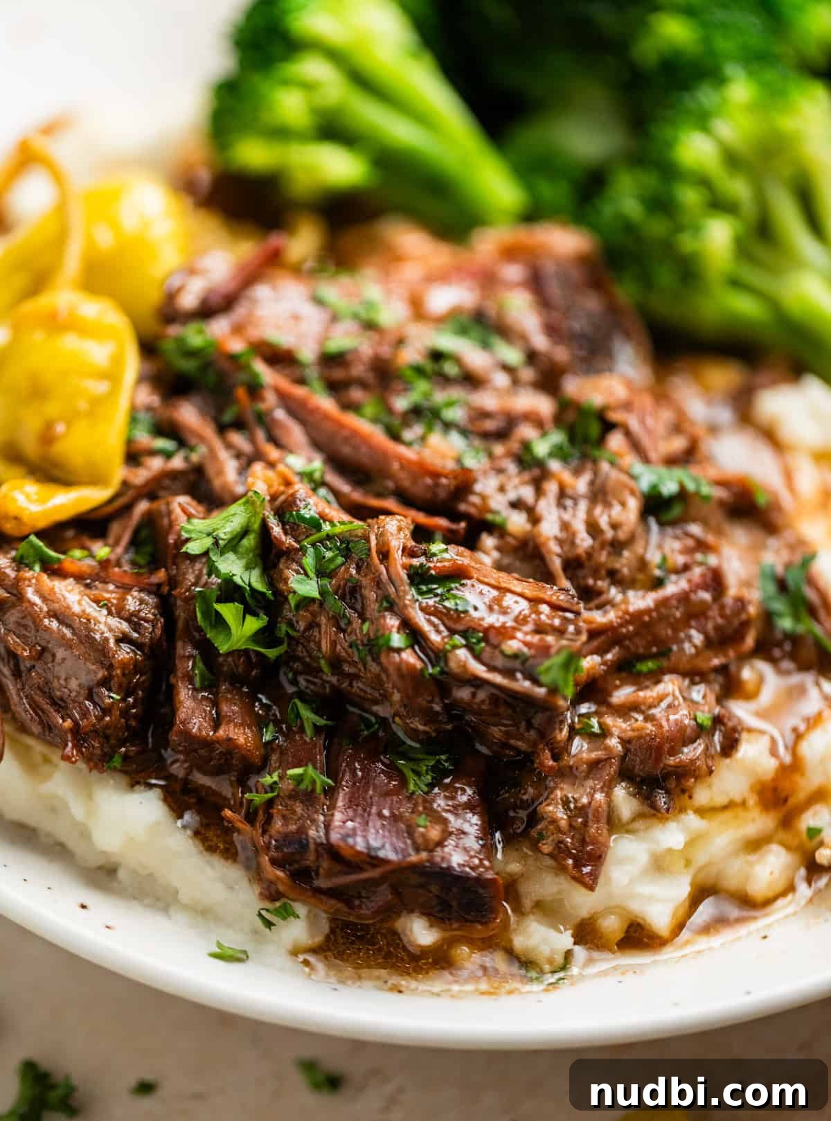 Mississippi Pot Roast in a Slow Cooker: Tender, Flavorful Recipe 2 Mississippi pot roast beef served over mashed potatoes with broccoli and pepperoncini peppers in the background.