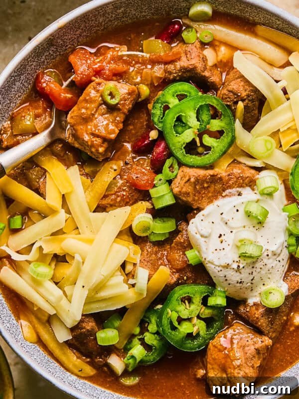 Mississippi Pot Roast in a Slow Cooker: Tender, Flavorful Recipe 10 Bowl of chili with brisket, shredded cheese, sour cream and spoon scooping up a spoonful.
