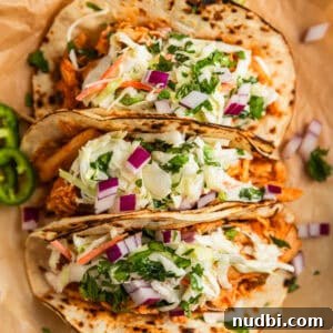 Slow Cooker BBQ Chicken Tacos with Crunchy Lime Slaw 11 BBQ chicken tacos topped with slaw and chopped cilantro and red onion on parchment.