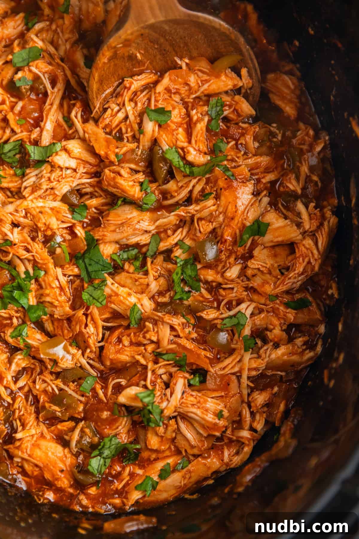 Slow Cooker BBQ Chicken Tacos with Crunchy Lime Slaw 9 Shredded bbq chicken topped with chopped cilantro in crockpot with wooden spoon scooping in.