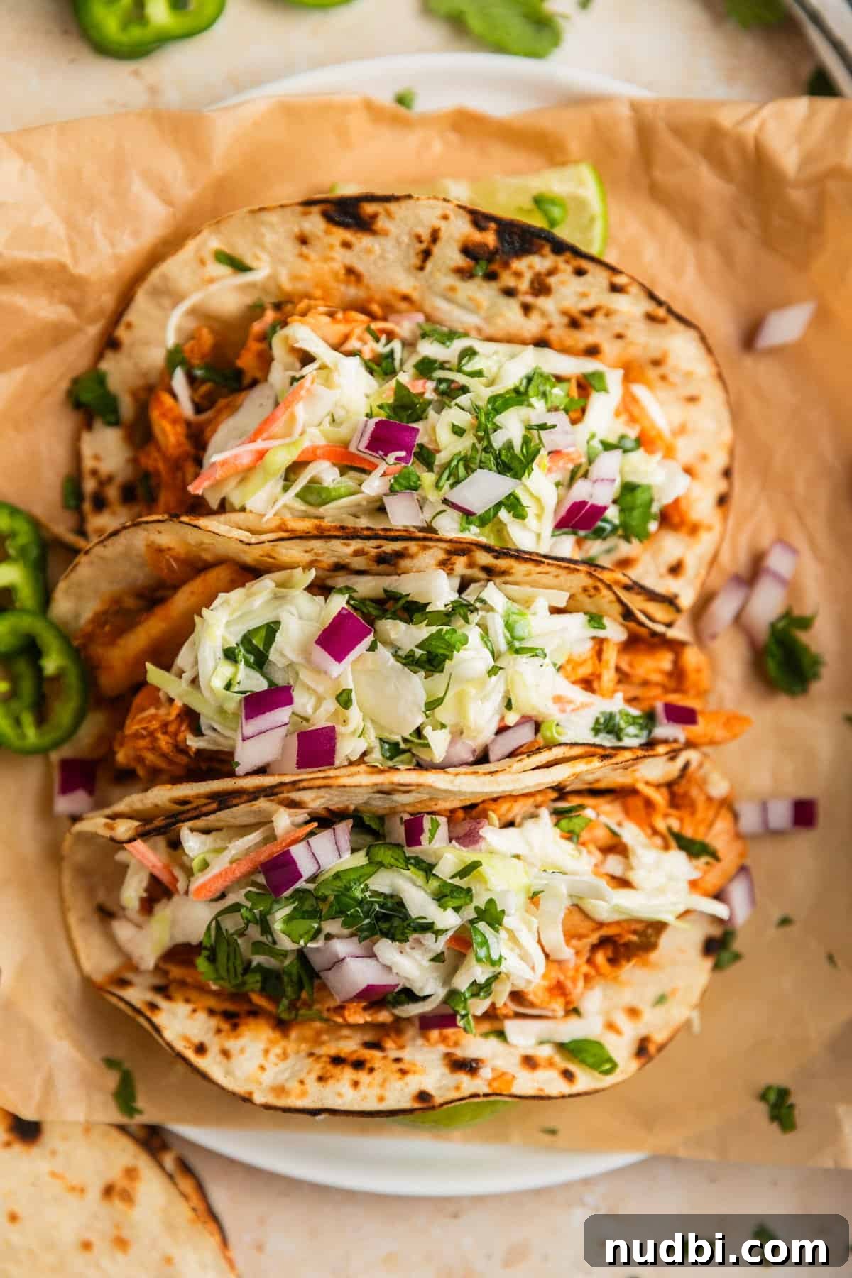 Slow Cooker BBQ Chicken Tacos with Crunchy Lime Slaw 10 Three chicken tacos on parchment topped with cole slaw.