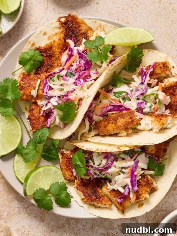 Crispy Air Fryer Salmon Bites with Lemon Garlic Dip 11 Air fryer fish tacos on white plate with lime and cilantro over top.