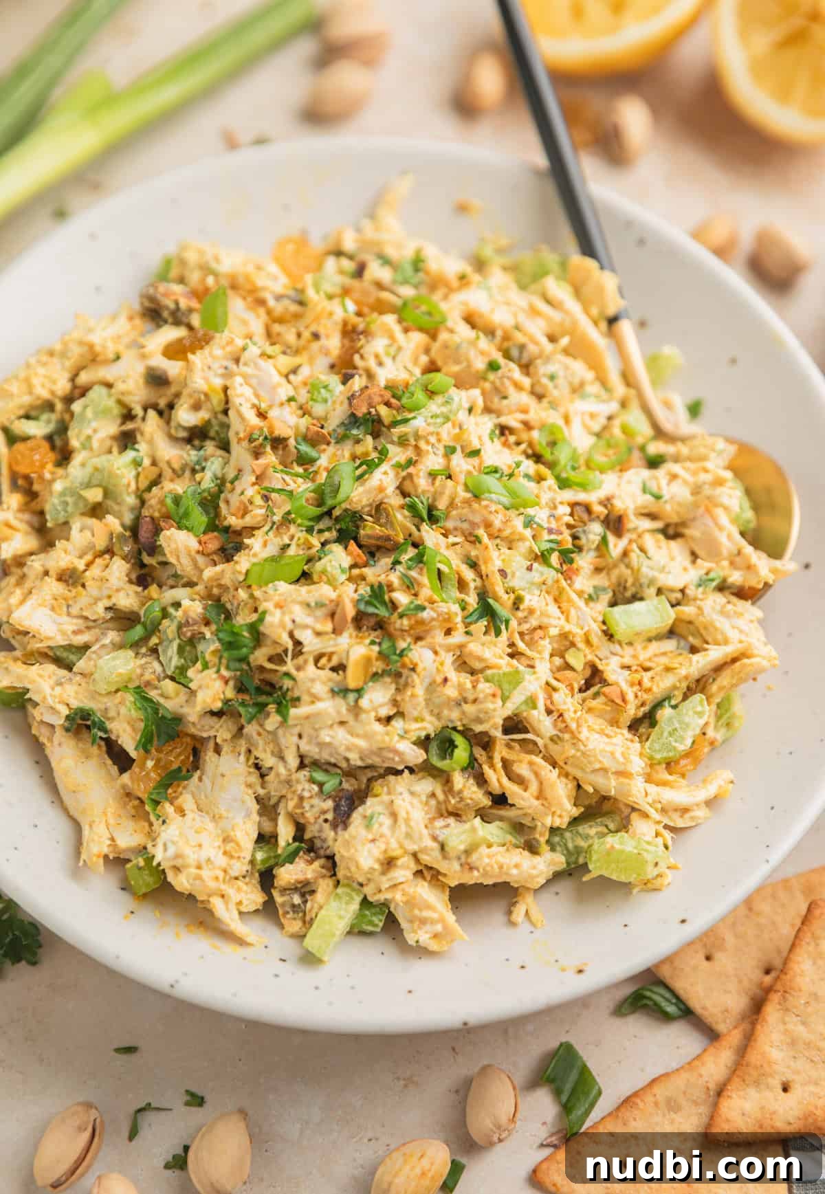 Creamy Curry Chicken Salad Recipe for Lunch or Light Dinner 2 Curry chicken salad in dish with spoon topped with chopped green onion, chopped pistachios and parsley.