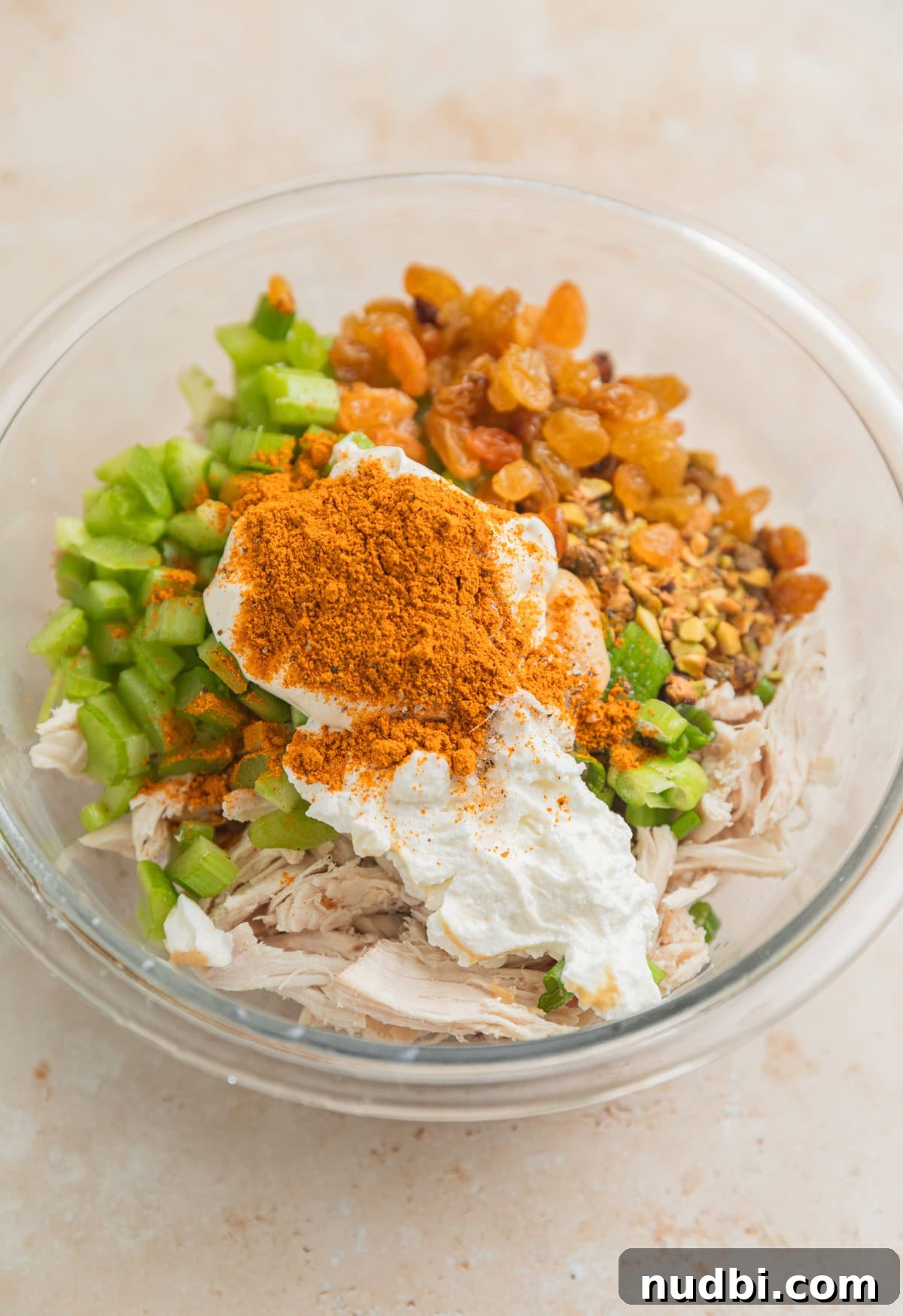 Creamy Curry Chicken Salad Recipe for Lunch or Light Dinner 4 Shredded chicken, celery, golden raisins, curry powder and other chicken salad ingredients in glass bowl.